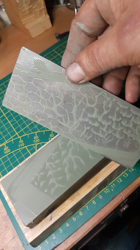 Groene synthetische waterwetsteen, met in de hand een diamant wetschijfje om de steen te vlakken.